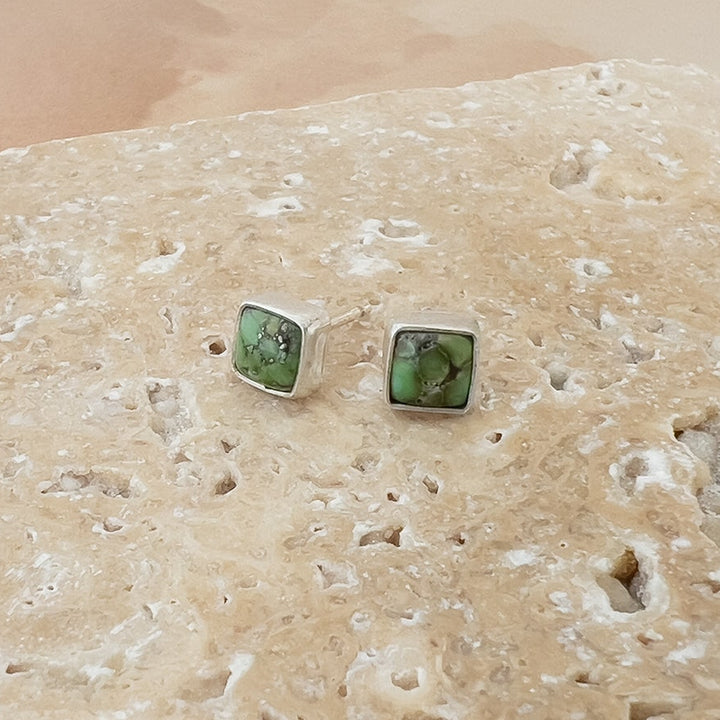 Close-up of squate Sonoran Gold Turquoise stud earrings set in polished sterling silver bezels on a neutral stone background.