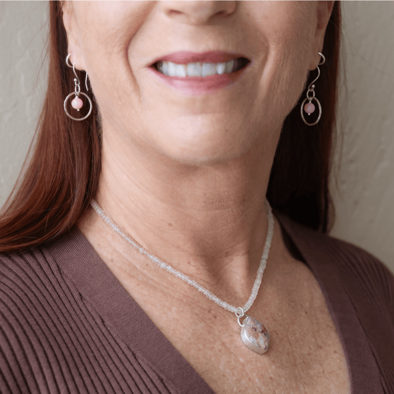 Woman wearing the Laguna Lace Agate and Rose Quartz Necklace by Novaura Jewelry and the Pink Flake Moonstone Open Circle Earrings with a neutral background