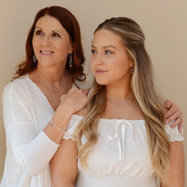 Mother embracing daughter - both wearing the Trinity Reflections Silver Necklaces.  A modern necklace with a subtle hammered texture and three interlocking circles on a sterling silver chain. Adjustable from 15 to 16 inches for a choker length.