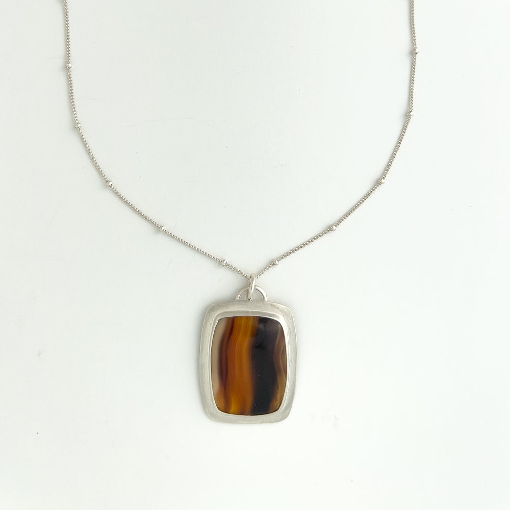 Montana Agate and Sterling Silver Pendant Necklace. Featuring a unique striped pattern of vibrant browns, creams, and shimmering gold,.