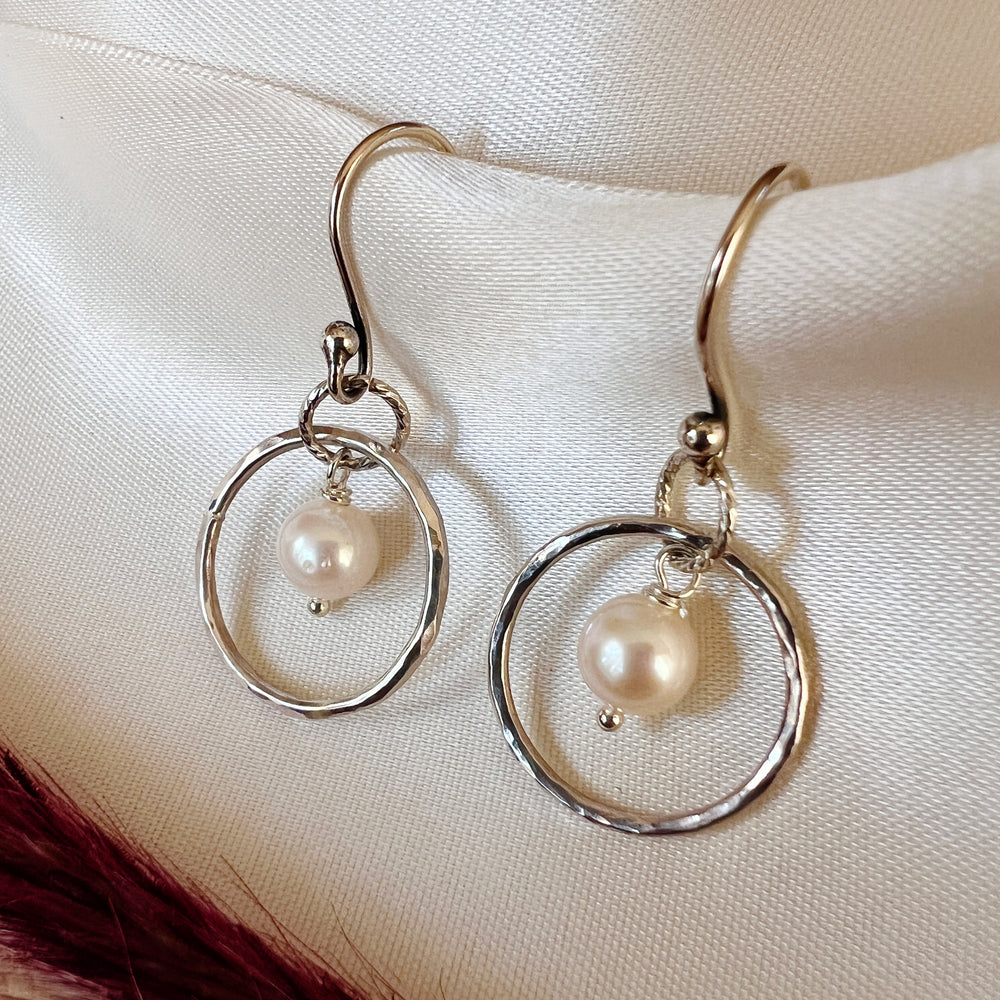 Elegantly crafted small sterling silver hoops adorned with delicate freshwater pearls and a shimmery hammered texture. Perfect for adding a touch of simple elegance to any outfit.