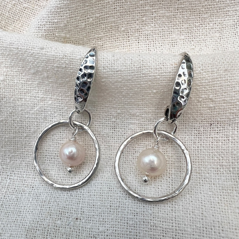 Elegantly crafted small sterling silver hoops adorned with delicate freshwater pearls and a shimmery hammered texture. Perfect for adding a touch of simple elegance to any outfit.