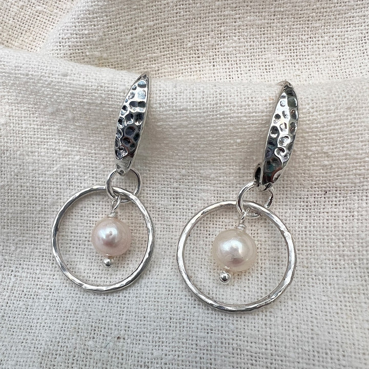 Elegantly crafted small sterling silver hoops adorned with delicate freshwater pearls and a shimmery hammered texture. Perfect for adding a touch of simple elegance to any outfit.