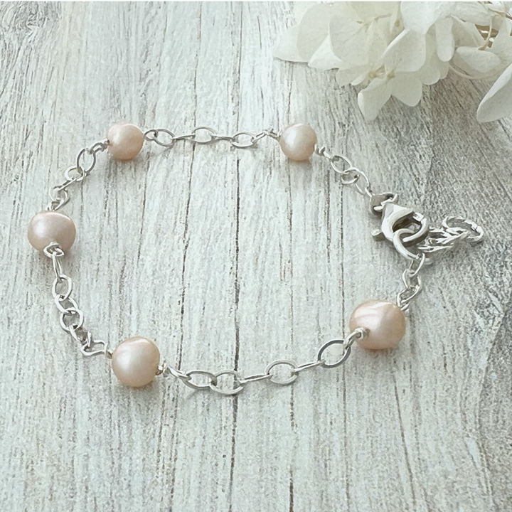 Freshwater pearl and sterling silver bracelet with creamy pearls and oval chain on wood background, showcasing soft luster and clasp detail.