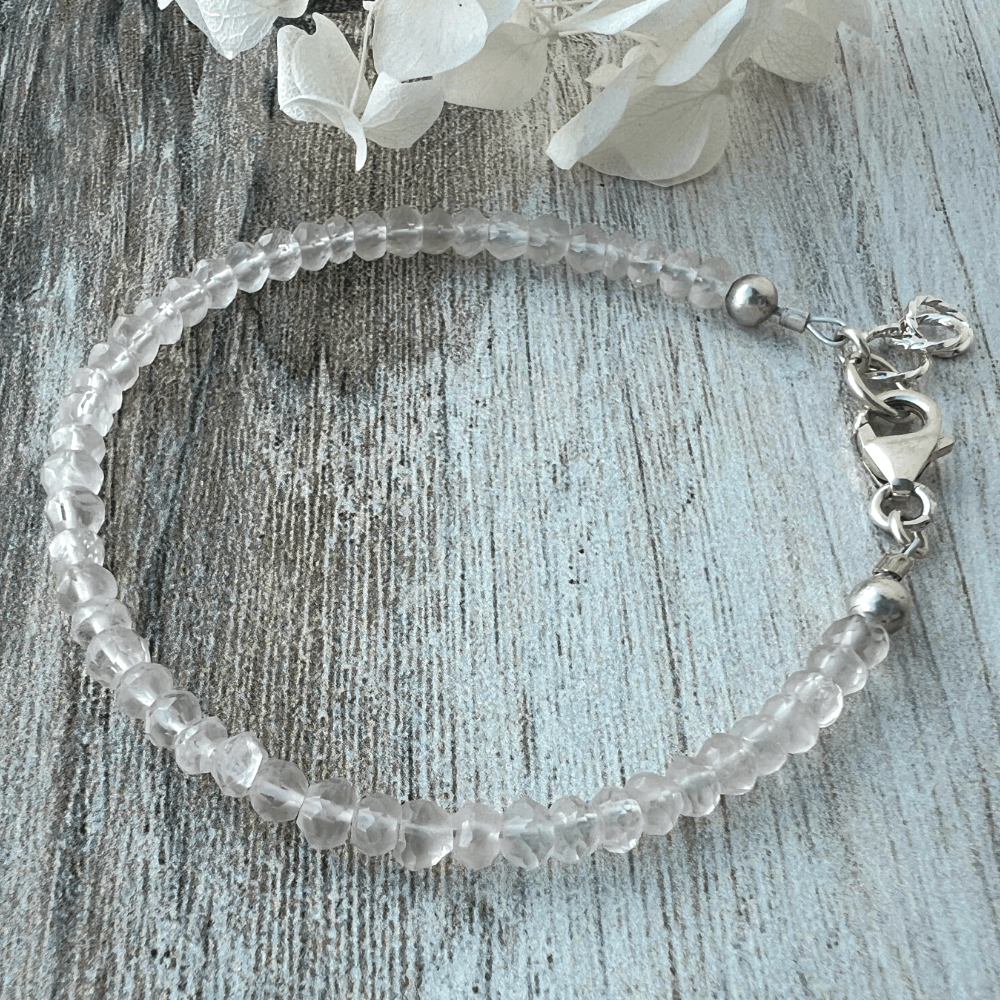 Rose Quartz beaded bracelet with a sterling silver lobster clasp on a textured wood surface.