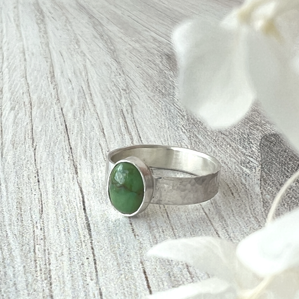 Close-up of a hand-hammered sterling silver ring featuring an oval Sonoran Gold Turquoise gemstone, photographed on a light wood surface with soft natural light.