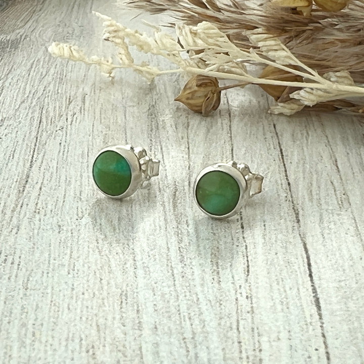 Close-up of round Sonoran Gold Turquoise stud earrings set in polished sterling silver bezels on a neutral stone background.