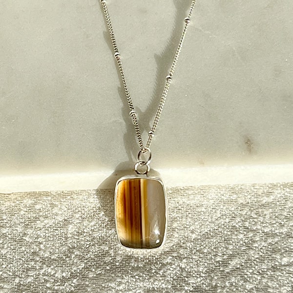 Stay stylish and chic in the Fall season with this Montana Agate & Sterling Silver Pendant Necklace. Featuring a striped pattern, this necklace is sure to make a bold impression! Crafted with a stunning Montana Agate and Sterling Silver, this is the perfect necklace to complete your Fall wardrobe.