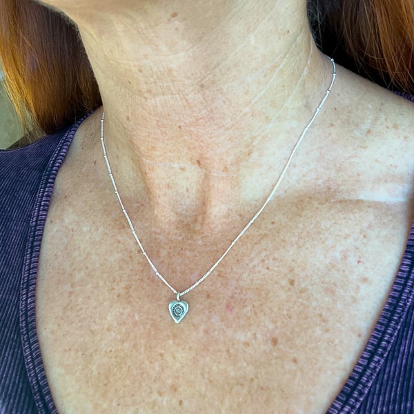Show your love with this romantic and feminine heart necklace. Crafted from fine silver and strung along an 18” dainty chain, it is the perfect way to add a touch of delicate beauty to your everyday look. Worn on model