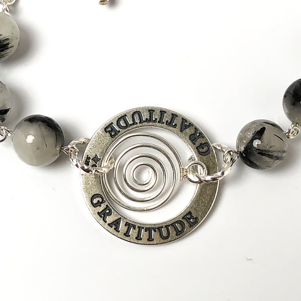 Is GRATITUDE your affirmation this year? This highly polished sterling silver circle charm is engraved on both sides and the lovely spiral drop gives it some whimsey. Milky white quartz with striking black needle-like inclusions of black tourmaline.  Handcrafted in CA. Detail of GRATITUDE charm.