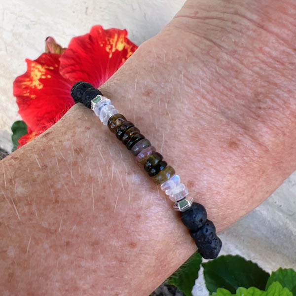 Heishi Shaped Tourmalines framed by Rainbow Moonstones highlight the translucent green and amber colors. Lava stone beads can absorb essential oil for relaxation. On wrist.